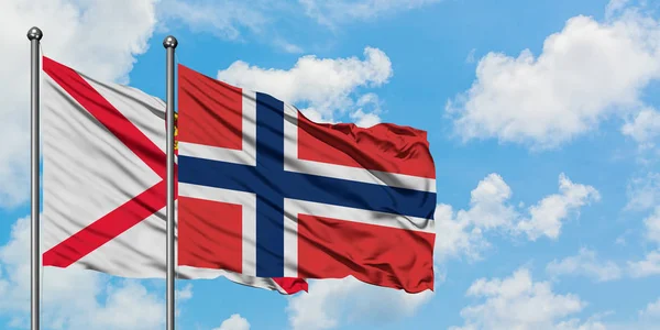 Jersey ve Norveç bayrağı birlikte beyaz bulutlu mavi gökyüzüne karşı rüzgarda sallayarak. Diplomasi kavramı, uluslararası ilişkiler. — Stok fotoğraf