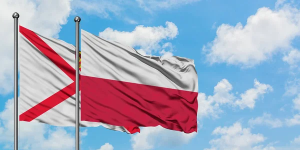 Jersey e la Polonia bandiera sventolando nel vento contro il cielo bianco nuvoloso blu insieme. Concetto di diplomazia, relazioni internazionali . — Foto Stock