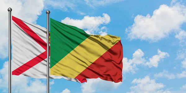 Bandera de Jersey y República del Congo ondeando en el viento contra el cielo azul nublado blanco juntos. Concepto diplomático, relaciones internacionales . — Foto de Stock