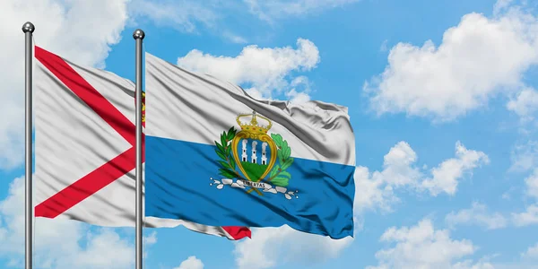 Bandera de Jersey y San Marino ondeando en el viento contra el cielo azul nublado blanco juntos. Concepto diplomático, relaciones internacionales . — Foto de Stock