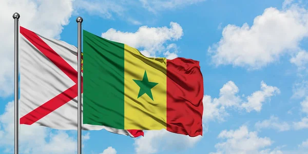 Bandera de Jersey y Senegal ondeando en el viento contra el cielo azul nublado blanco juntos. Concepto diplomático, relaciones internacionales . — Foto de Stock