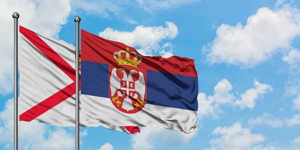 Bandera de Jersey y Serbia ondeando en el viento contra el cielo azul nublado blanco juntos. Concepto diplomático, relaciones internacionales . — Foto de Stock