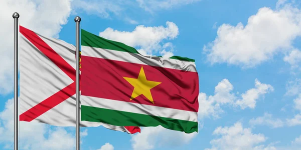 Bandera de Jersey y Surinam ondeando en el viento contra el cielo azul nublado blanco juntos. Concepto diplomático, relaciones internacionales . — Foto de Stock