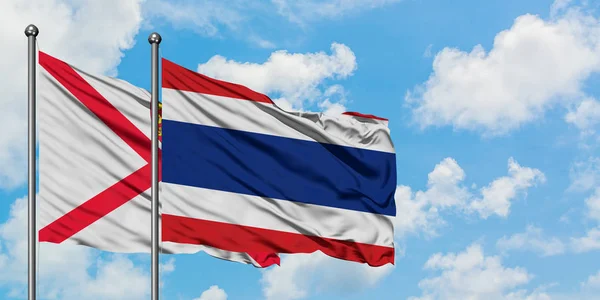 Bandera de Jersey y Tailandia ondeando en el viento contra el cielo azul nublado blanco juntos. Concepto diplomático, relaciones internacionales . — Foto de Stock