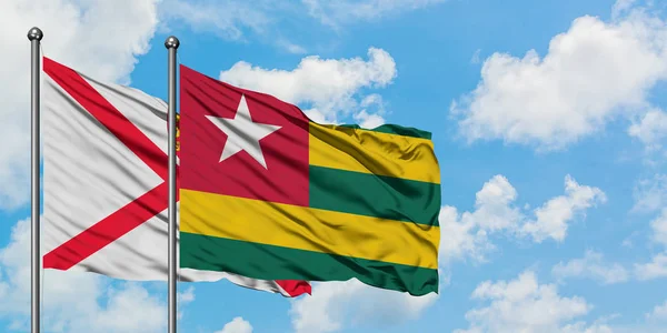 Bandera de Jersey y Togo ondeando en el viento contra el cielo azul nublado blanco juntos. Concepto diplomático, relaciones internacionales . — Foto de Stock
