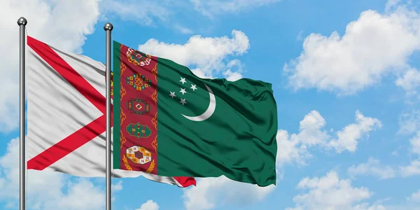 Bandera de Jersey y Turkmenistán ondeando en el viento contra el cielo azul nublado blanco juntos. Concepto diplomático, relaciones internacionales . — Foto de Stock