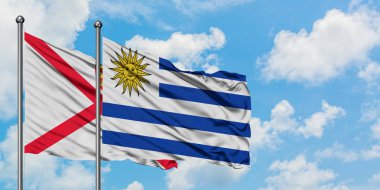 Jersey ve Uruguay bayrağı birlikte beyaz bulutlu mavi gökyüzüne karşı rüzgarda sallayarak. Diplomasi kavramı, uluslararası ilişkiler.
