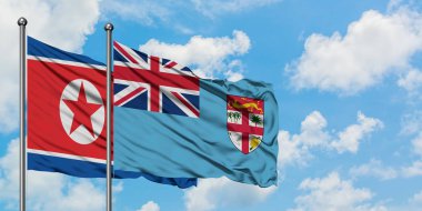 Kuzey Kore ve Fiji bayrağı birlikte beyaz bulutlu mavi gökyüzüne karşı rüzgarda sallayarak. Diplomasi kavramı, uluslararası ilişkiler.