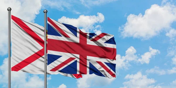 Jersey och Storbritannien flagga vifta i vinden mot vit grumlig blå himmel tillsammans. Diplomatisk koncept, internationella relationer. — Stockfoto