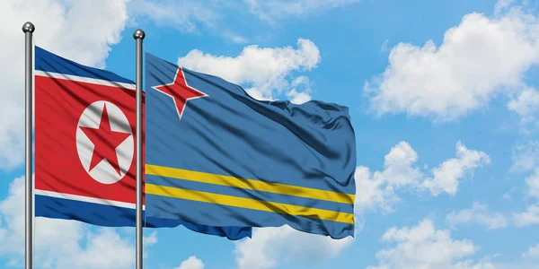 Corea del Norte y la bandera de Aruba ondeando en el viento contra el cielo azul nublado blanco juntos. Concepto diplomático, relaciones internacionales . —  Fotos de Stock