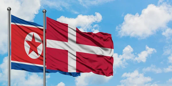 Bandera de Corea del Norte y Dinamarca ondeando en el viento contra el cielo azul nublado blanco juntos. Concepto diplomático, relaciones internacionales . —  Fotos de Stock
