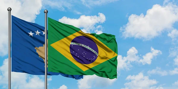 Bandera de Kosovo y Brasil ondeando en el viento contra el cielo azul nublado blanco juntos. Concepto diplomático, relaciones internacionales . — Foto de Stock