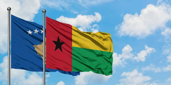 Bandera de Kosovo y Guinea Bissau ondeando en el viento contra el cielo azul nublado blanco juntos. Concepto diplomático, relaciones internacionales . — Foto de Stock