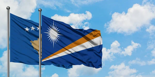 A bandeira do Kosovo e das Ilhas Marshall agitando no vento contra o céu azul nublado branco juntos. Conceito de diplomacia, relações internacionais . — Fotografia de Stock