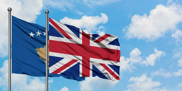 Bandera de Kosovo y el Reino Unido ondeando en el viento contra el cielo azul nublado blanco juntos. Concepto diplomático, relaciones internacionales . — Foto de Stock