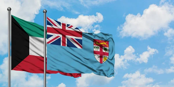 Bandera de Kuwait y Fiyi ondeando en el viento contra el cielo azul nublado blanco juntos. Concepto diplomático, relaciones internacionales . — Foto de Stock