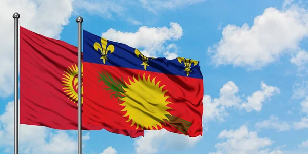 Bandera de Kirguistán y Guadalupe ondeando en el viento contra el cielo azul nublado blanco juntos. Concepto diplomático, relaciones internacionales . — Foto de Stock
