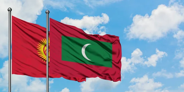 Bandera de Kirguistán y Maldivas ondeando en el viento contra el cielo azul nublado blanco juntos. Concepto diplomático, relaciones internacionales . — Foto de Stock