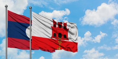 Laos ve Cebelitarık bayrağı birlikte beyaz bulutlu mavi gökyüzüne karşı rüzgarda sallayarak. Diplomasi kavramı, uluslararası ilişkiler.