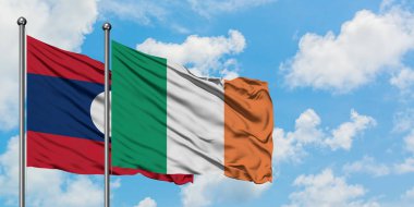 Laos ve İrlanda bayrağı birlikte beyaz bulutlu mavi gökyüzüne karşı rüzgarda sallayarak. Diplomasi kavramı, uluslararası ilişkiler.