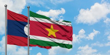 Laos ve Surinam bayrağı birlikte beyaz bulutlu mavi gökyüzüne karşı rüzgarda sallayarak. Diplomasi kavramı, uluslararası ilişkiler.