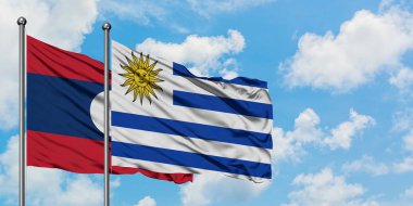 Laos ve Uruguay bayrağı birlikte beyaz bulutlu mavi gökyüzüne karşı rüzgarda sallayarak. Diplomasi kavramı, uluslararası ilişkiler.