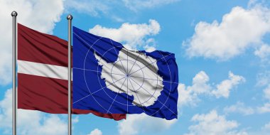 Letonya ve Antarktika bayrağı birlikte beyaz bulutlu mavi gökyüzüne karşı rüzgarda sallayarak. Diplomasi kavramı, uluslararası ilişkiler.