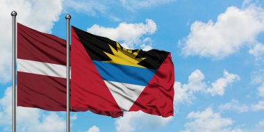 Letonya ve Antigua ve Barbuda bayrağı birlikte beyaz bulutlu mavi gökyüzüne karşı rüzgarda sallayarak. Diplomasi kavramı, uluslararası ilişkiler.
