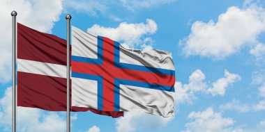 Letonya ve Faroe Adaları bayrağı birlikte beyaz bulutlu mavi gökyüzüne karşı rüzgarda sallayarak. Diplomasi kavramı, uluslararası ilişkiler.