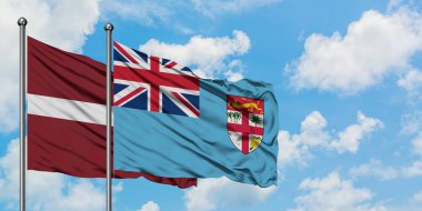 Letonya ve Fiji bayrağı birlikte beyaz bulutlu mavi gökyüzüne karşı rüzgarda sallayarak. Diplomasi kavramı, uluslararası ilişkiler.