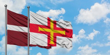 Letonya ve Guernsey bayrağı birlikte beyaz bulutlu mavi gökyüzüne karşı rüzgarda sallayarak. Diplomasi kavramı, uluslararası ilişkiler.