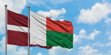 Letonya ve Madagaskar bayrağı birlikte beyaz bulutlu mavi gökyüzüne karşı rüzgarda sallayarak. Diplomasi kavramı, uluslararası ilişkiler.