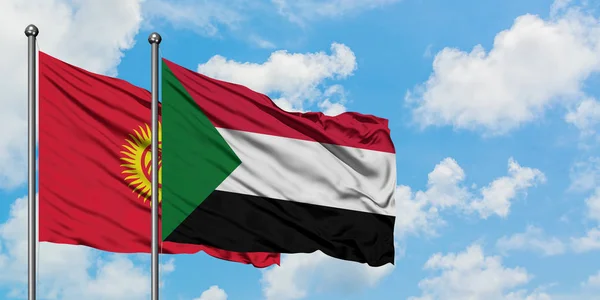 Bandera de Kirguistán y Sudán ondeando en el viento contra el cielo azul nublado blanco juntos. Concepto diplomático, relaciones internacionales . — Foto de Stock