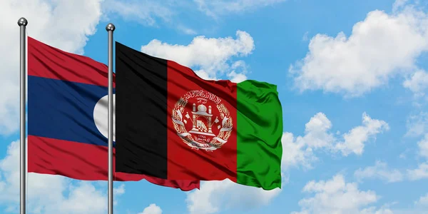 Laos y la bandera de Afganistán ondeando en el viento contra el cielo azul nublado blanco juntos. Concepto diplomático, relaciones internacionales . — Foto de Stock