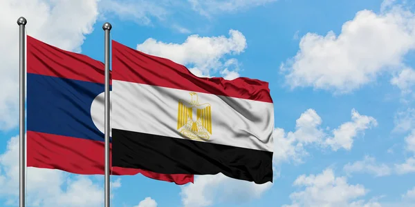 Bandera de Laos y Egipto ondeando en el viento contra el cielo azul nublado blanco juntos. Concepto diplomático, relaciones internacionales . — Foto de Stock