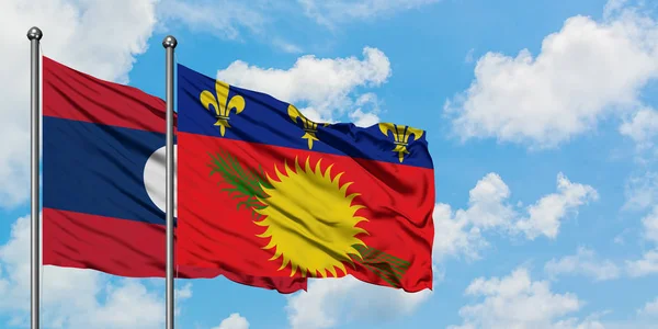 Bandera de Laos y Guadalupe ondeando en el viento contra el cielo azul nublado blanco juntos. Concepto diplomático, relaciones internacionales . — Foto de Stock