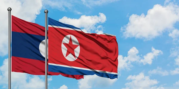 Η σημαία του Λάος και της Βόρειας Κορέας κουνώντας τον άνεμο ενάντια στον λευκό θολό γαλάζιο ουρανό μαζί. Φιλοσοφία της διπλωματίας, διεθνείς σχέσεις. — Φωτογραφία Αρχείου