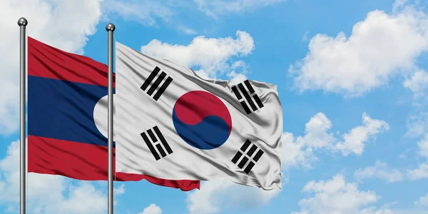 Laos ve Güney Kore bayrağı birlikte beyaz bulutlu mavi gökyüzüne karşı rüzgarsal sallayarak. Diplomasi kavramı, uluslararası ilişkiler. — Stok fotoğraf