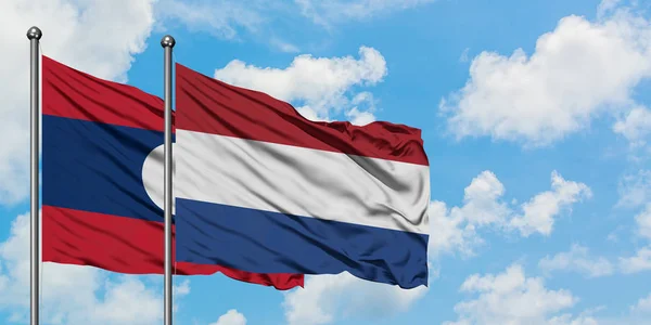 Laos e bandiera olandese sventolano insieme nel vento contro il bianco cielo blu nuvoloso. Concetto di diplomazia, relazioni internazionali . — Foto Stock