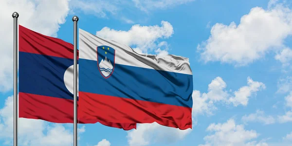 Laos and Slovenia flag waving in the wind against white cloudy blue sky together. Diplomacy concept, international relations. — Stock Photo, Image