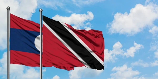 Laos ve Trinidad ve Tobago bayrağı birlikte beyaz bulutlu mavi gökyüzüne karşı rüzgarda sallayarak. Diplomasi kavramı, uluslararası ilişkiler. — Stok fotoğraf