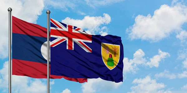 Bandera de Laos y las Islas Turcas y Caicos ondeando en el viento contra el cielo azul nublado blanco juntos. Concepto diplomático, relaciones internacionales . — Foto de Stock