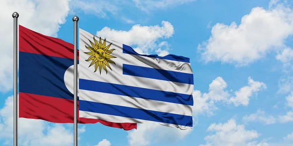 Bandera de Laos y Uruguay ondeando en el viento contra el cielo azul nublado blanco juntos. Concepto diplomático, relaciones internacionales . —  Fotos de Stock