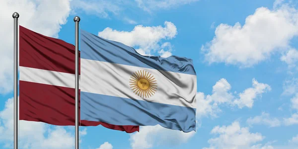 Bandera de Letonia y Argentina ondeando en el viento contra el cielo azul nublado blanco juntos. Concepto diplomático, relaciones internacionales . — Foto de Stock