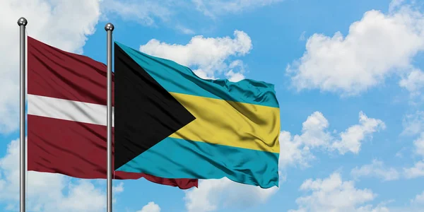 Łotwa i Bahamy flaga machając w wiatr przed białym zachmurzone błękitne niebo razem. Koncepcja dyplomacji, stosunki międzynarodowe. — Zdjęcie stockowe