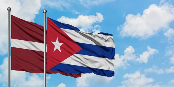 Letônia e Cuba acenando com a bandeira no vento contra o céu azul nublado branco juntos. Conceito de diplomacia, relações internacionais . — Fotografia de Stock