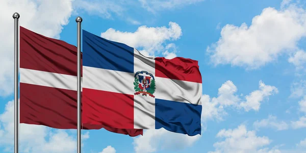 Lettland und die Dominikanische Republik schwenken gemeinsam die Flagge im Wind vor dem wolkenverhangenen blauen Himmel. Diplomatie-Konzept, internationale Beziehungen. — Stockfoto