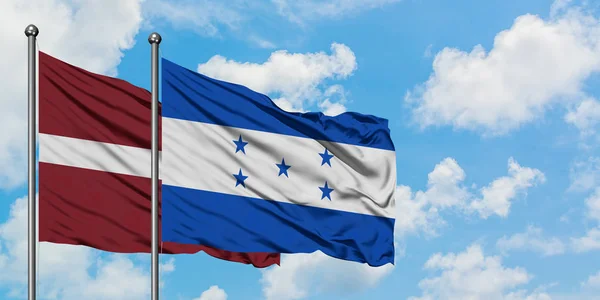 Bandera de Letonia y Honduras ondeando en el viento contra el cielo azul nublado blanco juntos. Concepto diplomático, relaciones internacionales . — Foto de Stock