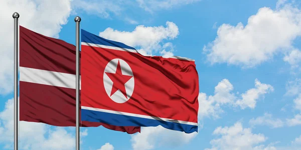 라트비아와 북한 국기가 하얀 흐린 푸른 하늘을 배경으로 바람에 흔들리고 있다. 외교 개념, 국제 관계. — 스톡 사진
