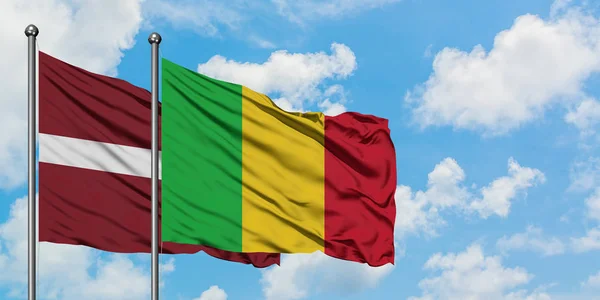 Łotwa i Mali flagi machając w wiatr przed białym zachmurzone błękitne niebo razem. Koncepcja dyplomacji, stosunki międzynarodowe. — Zdjęcie stockowe